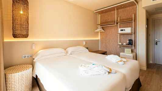 Ett hotellrum med en dubbelsäng, ljus inredning och en flätad lampa hängande på väggen. (AI-genererad text)