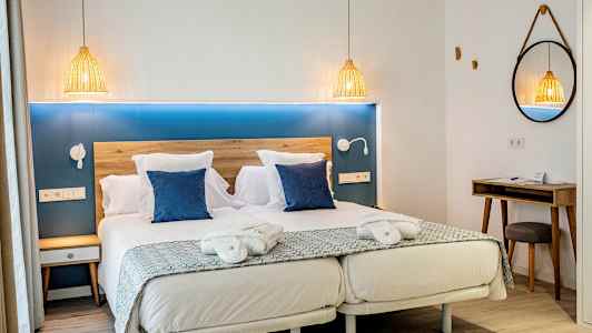 Ett hotellrum med en dubbelsäng, två blå kuddar, nattduksbord och en spegel. (AI-genererad text)