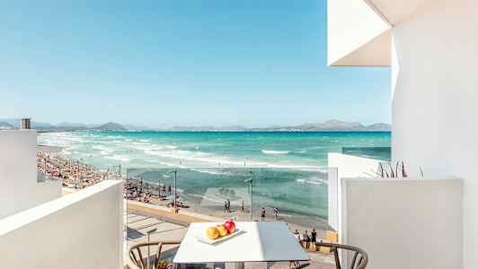 Utsikt från en balkong mot en strand med turkost vatten, sand och människor som badar. (AI-genererad text)