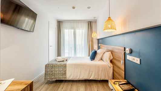 Ett hotellrum med en dubbelsäng, en blå väggpanel, en TV på väggen och naturliga träytor. (AI-genererad text)