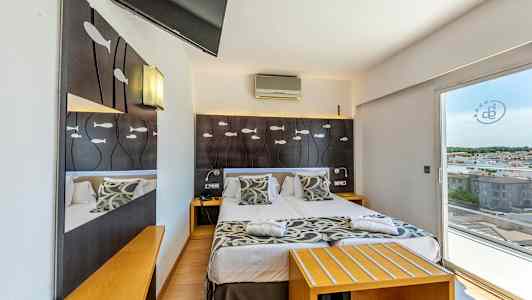 Hotellrum med dubbelsäng, dekorerat med fiskmotiv på sänggaveln och en utsikt mot staden genom glasdörrar. (AI-genererad text)