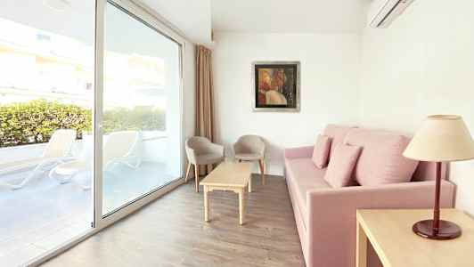 Soffa med rosa klädsel, vardagsrumsbord, två stolar och fönster med utsikt mot terrassen. (AI-genererad text)