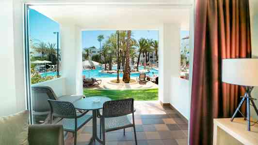 Utsikt från ett rum med balkong mot en solig poolområde. (AI-genererad text)