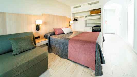 Ett hotellrum med en dubbelsäng, en soffa och en öppen garderob. (AI-genererad text)