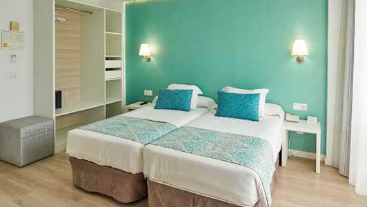 Ett hotellrum med två enkelsängar, turkosa kuddar och väggar. (AI-genererad text)