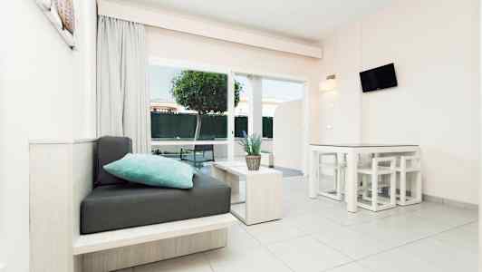 Ett modernt ljusrum med sittmöbler, bord och en växt, stora fönster och trädgårdsutsikt. (AI-genererad text)