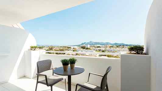 Balkong med bord och stolar, utsikt över omgivande byggnader och berg. (AI-genererad text)