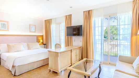 Hotellrum med dubbelsäng, TV, skrivbord och soffa. Balkong med utsikt. (AI-genererad text)