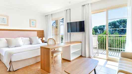 Ett hotellrum med en dubbelsäng, skrivbord och TV. Stora glasdörrar leder ut till en balkong. (AI-genererad text)