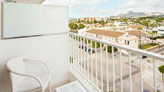 En balkong med två vita stolar och ett bord, med utsikt över en gata och byggnader. (AI-genererad text)