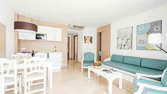 Bilden visar ett ljust och modernt möblerat vardagsrum med köksvrå och matplats. (AI-genererad text)