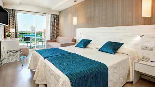 Hotellrum med två sängar, en soffa och en glasbalkong. (AI-genererad text)