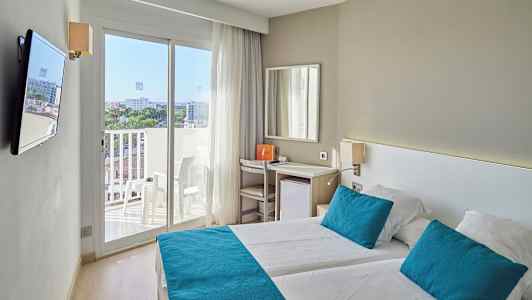 Ett ljust hotellrum med två sängar, blåa kuddar och överkast, samt en balkong med utsikt. (AI-genererad text)