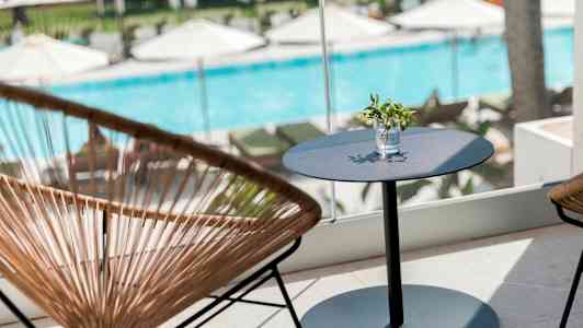 En sittgrupp med ett bord och stolar framför ett fönster med utsikt över en pool och solstolar. (AI-genererad text)