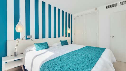 Ett sovrum med en säng, blå randig vägg och vita möbler. (AI-genererad text)