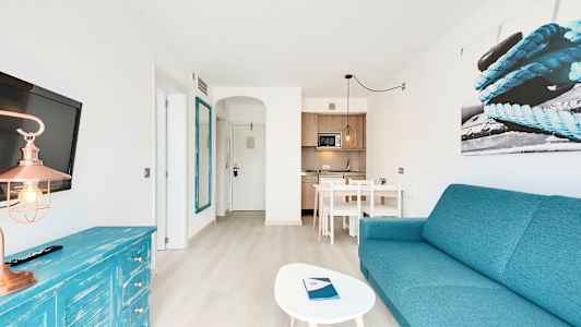 Ett ljust hotellrum med turkost tema, inklusive soffa, bord, tv och pentry. (AI-genererad text)