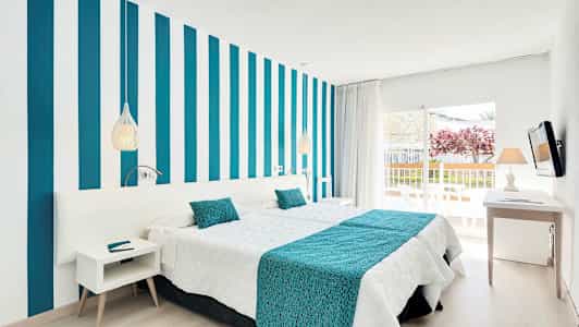 Ett modernt hotellrum med randig vägg, vita och turkosa sängkläder samt en balkong med utsikt. (AI-genererad text)