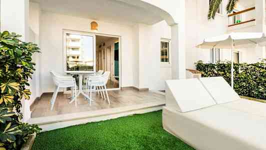 Uteplats med bord och stolar samt solstolar och parasoll vid gräsmatta. (AI-genererad text)