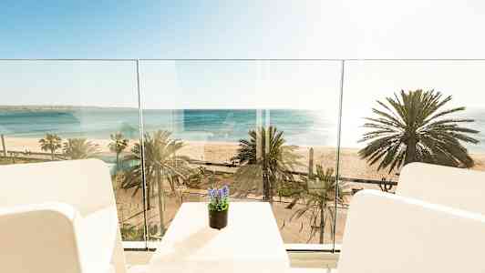 Utsikt från en balkong mot havet och stranden med palmer. (AI-genererad text)