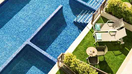 Bild av en swimmingpool med blå mosaik, två solstolar och ett bord med stolar på en grönyta. (AI-genererad text)