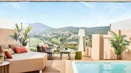 En terrass med utsikt över en grön dal och hus i fjärran, med sittmöbler och en liten pool. (AI-genererad text)