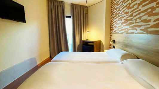 Två enkelsängar i ett hotellrum med ett mönstrat huvudgavel och en TV på väggen. (AI-genererad text)