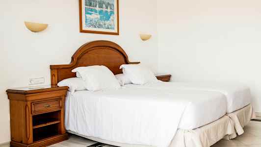 Ett sovrum med två enkelsängar, trä sänggavel, och ett nattduksbord. (AI-genererad text)