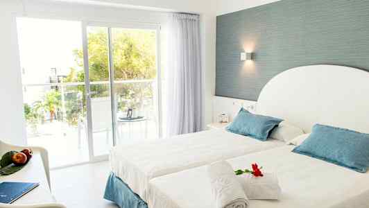 Hotellrum med bäddad säng och insläpp av dagsljus genom stora glasdörrar. (AI-genererad text)
