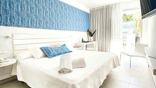 Bild på ett ljust hotellrum med en dubbelsäng, vita möbler och detaljer i blått. (AI-genererad text)