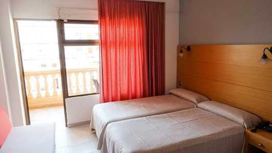 Hotellrum med två enkelsängar, röd gardin och balkong. (AI-genererad text)