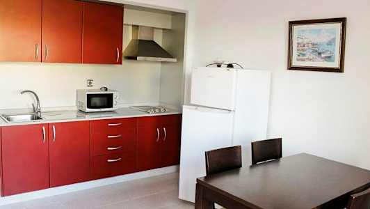 Ett kök med röda skåp, ett kylskåp och en matplats med ett bord och stolar. (AI-genererad text)