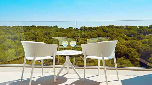 Två vita stolar vid ett runt bord med två glas på en altan med utsikt över ett skogsklätt landskap. (AI-genererad text)