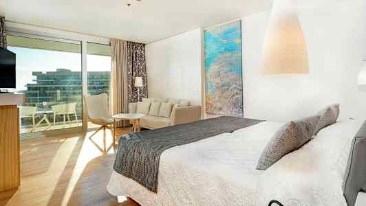 Modernt hotellrum med stor säng, sittgrupp och utgång till balkong. (AI-genererad text)