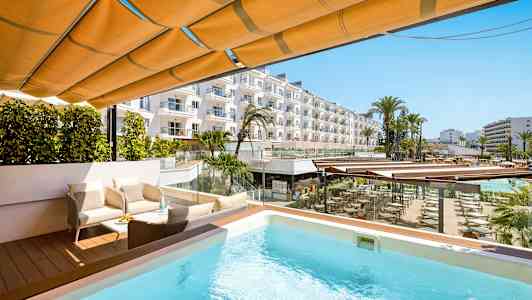 Terrass med pool, sittgrupp och utsikt över hotellområde med palmer och byggnader. (AI-genererad text)