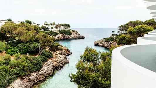 Utsikt över en vik med klart vatten, gröna träd och vita byggnader. (AI-genererad text)