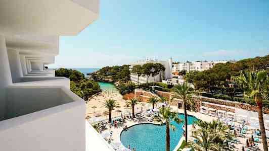 Utsikt från en balkong mot ett hotellområde med pool, strand och träd. (AI-genererad text)