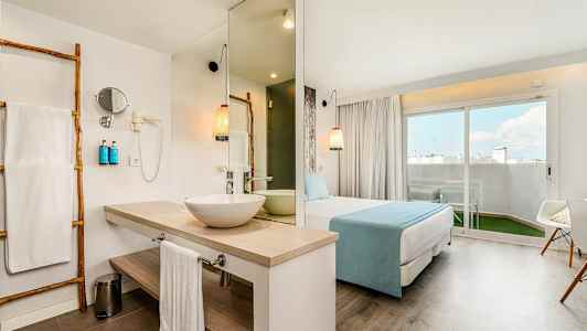 Hotellrum med badrum, sovdel och sittgrupp. Stor fönsterdörr mot en utomhusterrass. (AI-genererad text)