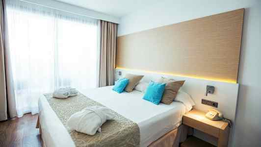 Ett modernt hotellrum med en dubbelsäng, två badrockar och en telefon på nattduksbordet. (AI-genererad text)