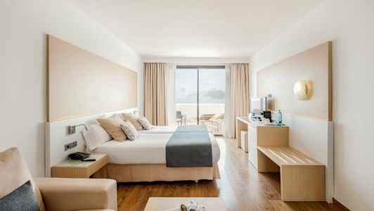 Modernt hotellrum med dubbelsäng och utsikt mot terrass och hav. (AI-genererad text)