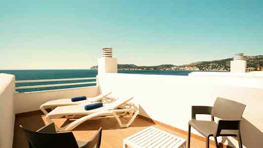 En terrass med solstolar, ett bord och två stolar samt utsikt över havet och omgivande landskap. (AI-genererad text)