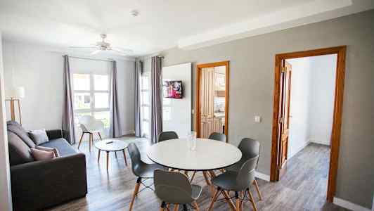 Ett vardagsrum med grå soffa, matbord med stolar, och en TV på väggen. (AI-genererad text)