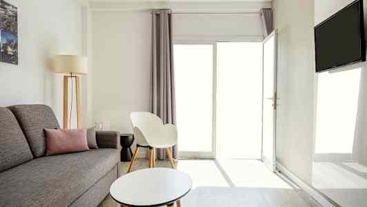 Ett ljust och modernt inrett vardagsrum med grå soffa, en vit stol och ett runt soffbord. (AI-genererad text)