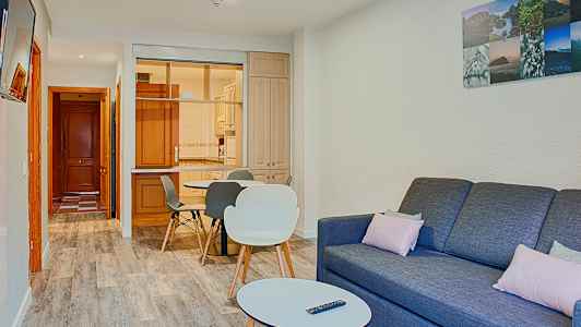 Ett vardagsrum med en soffa, ett soffbord och en matplats nära ett kök. (AI-genererad text)