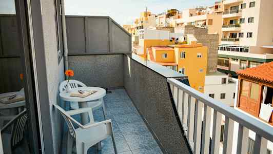 En balkong med utsikt över omkringliggande byggnader. Det finns ett bord med två stolar, en bok och en blomma på bordet. (AI-genererad text)