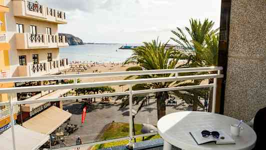 Utsikt från ett hotellrum med en balkong mot en strand och havet. (AI-genererad text)