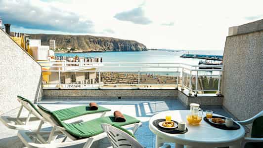 Terrass med två solsängar och en bord med orangejuice och bakverk, havsutsikt i bakgrunden. (AI-genererad text)