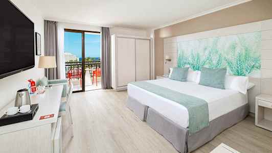 Modernt hotellrum med dubbelsäng, skrivbord, TV och balkong med utsikt. (AI-genererad text)