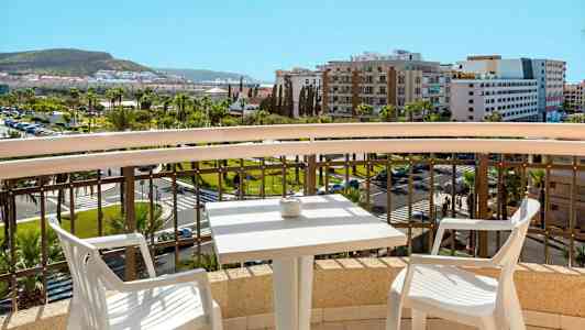 Utsikt från en balkong med ett bord och två stolar, över en stad och grönområden. (AI-genererad text)