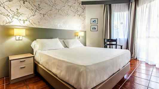 Ett rum med en dubbelsäng, nattduksbord, stol och fönster med gardiner. (AI-genererad text)