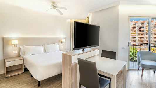 Ljusa sovrum med en dubbelsäng, ett bord med stolar och en stor TV framför sängen. (AI-genererad text)